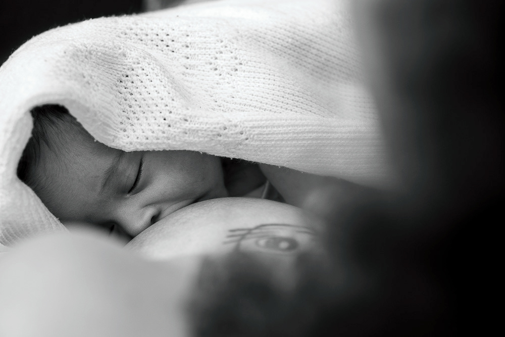 Black-and-white close-up of Anya nestled under a knit blanket. Águas Santas, Portugal. 2025 © Pedro Rodrigues